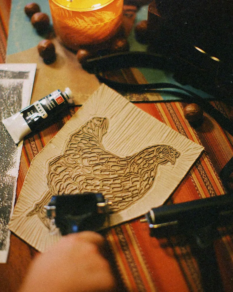 Bloc de linoléum gravé posé sur une table d’atelier, à côté d’un tube d’encre et d’une épreuve imprimée