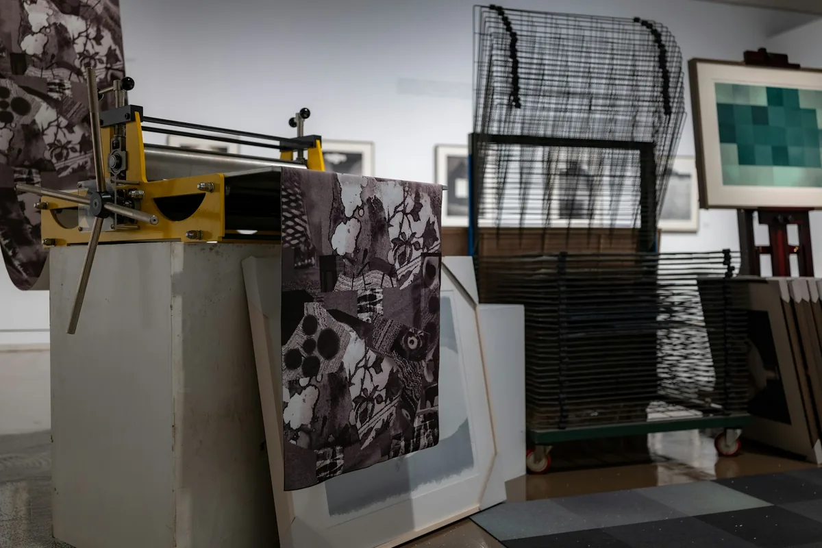 Presse à graver dans un atelier d’estampe, avec une feuille imprimée posée sur le plateau et un séchoir à claies en arrière-plan